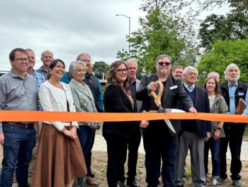 Mayor of Corvallis Charles Maughan surrounded by a crowd of officials holding a giant pair of scissors to cut an orange ribbon.