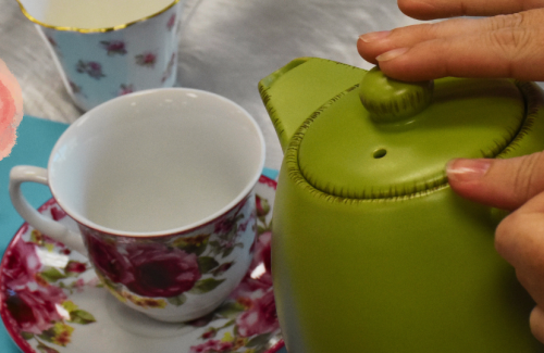 Tea kettle pouring tea into a teacup.