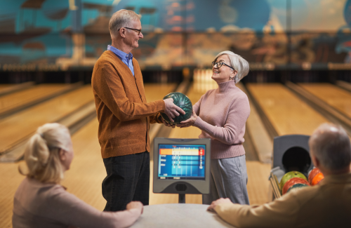 senior man hands senior woman a bowling ball