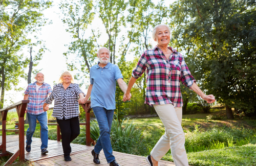 Four seniors holding hands, walking down an outdoor park path