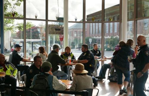 Police officers having coffee with community members at a local coffee shop on a sunny morning.