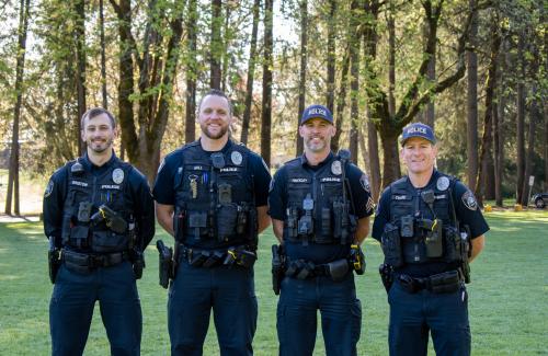 A group of four uniformed officers in front of trees