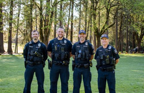 Four Officers stand outside in front of large trees smiling for a photo