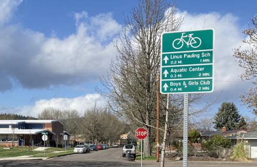 Neighborhood bikeways sign on a city street with cloudy blue sky in the background.