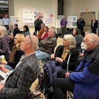 About 20 to 30 visitors in the Library meeting room listening to the speaker talk about the city facilities project