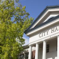 Corvallis City Hall with a green tree to the left, on a clear day with a sunny blue sky overhead.