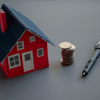 Miniature house next to a stack of coins and a pen