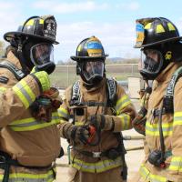 3 volunteer firefighters in yellow coats and breathing masks