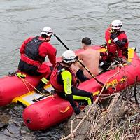 Two rescue swimmers on a red inflatable raft tend to a victim.