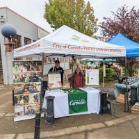 The Mayor and City Councilors behind a display table on a street corner at the Corvallis Farmers Market.