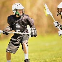 Two kids in black uniforms playing lacrosse