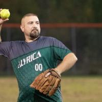 Coed softball game centered on man throwing ball