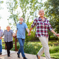 Four seniors holding hands, walking down an outdoor park path