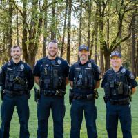 Four Officers stand outside in front of large trees smiling for a photo