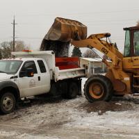 Yellow bucket loader putting sand in the back of a pickup truck.