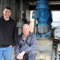 Two workers standing near some big pipes and valves at the wastewater plant. 