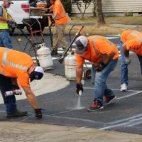City workers spraying street markings onto a newly paved street.