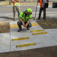Engineer kneeling to examine curb ramps on a sidewalk