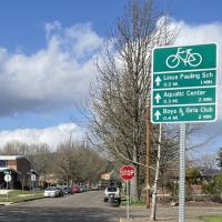 Neighborhood bikeways sign on a city street with cloudy blue sky in the background.