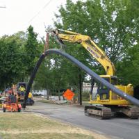 Yellow excavator on a city street installing pipe.
