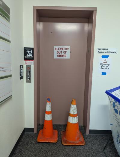 Elevator with an out of service sign and two orange hazard cones blocking the door