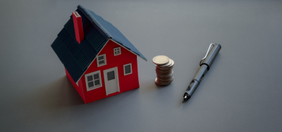 Miniature house next to a stack of coins and a pen