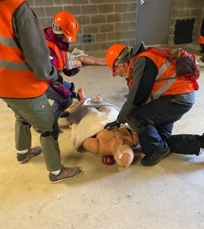 Volunteers wearing orange vests conducting first aid drills on a dummy lying on the ground.