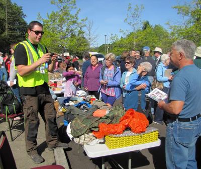 CERT volunteer in a bright yellow vest talking with neighbors at an outdoor rally point.