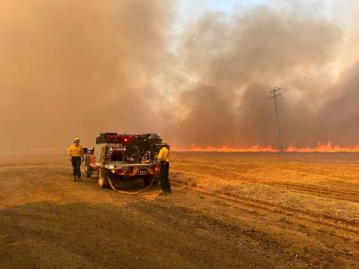 Corvallis firefighters with a small fire engine in a dry grass field, with a line of bright orange flames in the background