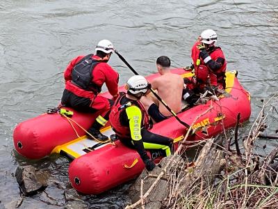 Two rescue swimmers on a red inflatable raft tend to a victim.