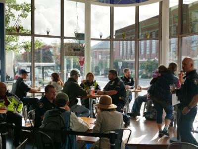 Police officers having coffee with community members at a local coffee shop on a sunny morning.