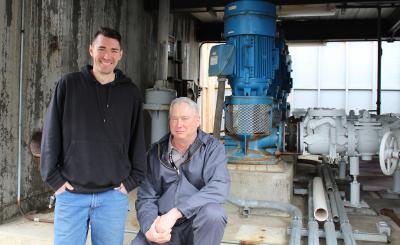 Two workers standing near some big pipes and valves at the wastewater plant. 