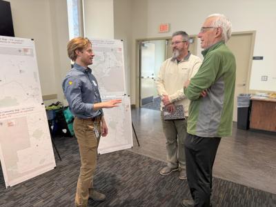 Three people standing around a stand-up easel engaged in a discussion about transportation safety.