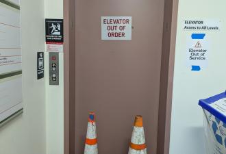 Elevator with an out of service sign and two orange hazard cones blocking the door