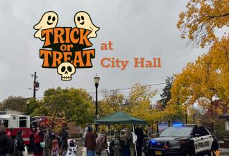 Costumed trick or treaters visiting City Hall on a cloudy day. A tree with yellow leaves hangs over the outdoor plaza.