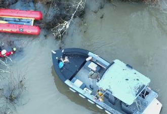 Two rescue boats on the Willamette River attempting to reach a kayaker near a submerged tree.