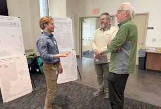 Three people standing around a stand-up easel engaged in a discussion about transportation safety.
