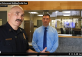 Video screenshot showing uniformed police chief speaking to the camera while standing in a public lobby