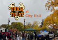 Costumed trick or treaters visiting City Hall on a cloudy day. A tree with yellow leaves hangs over the outdoor plaza.