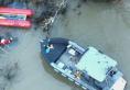 Two rescue boats on the Willamette River attempting to reach a kayaker near a submerged tree.
