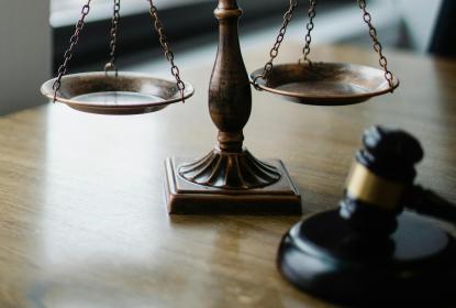 Scales of justice on a desk near an open window, with a gavel nearby.
