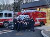 Firefighters standing in front of a red fire engine parked on a parking pad.